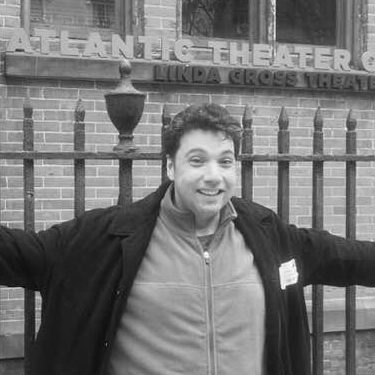 A man with outstretched arms in front of a theatre with the words Atlantic Theatre visible.
