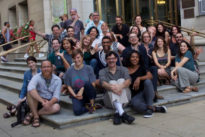 A group shot of about 20 people sitting on steps in front of a building