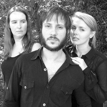 A black and white image of three actors, a man with a coloured shirt and two female actresses on the side of the male actor.