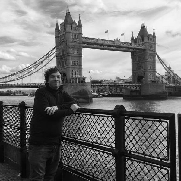 A man posing in front of a bridge. The bridge is Tower Bridge in London, UK.